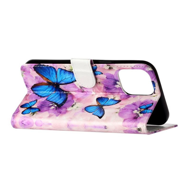 Housse iPhone 16 Pro Papillons Bleus et Fleurs Violettes à Lanière